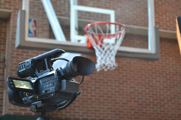 A video camera is set up with a basketball hoop hanging over it.