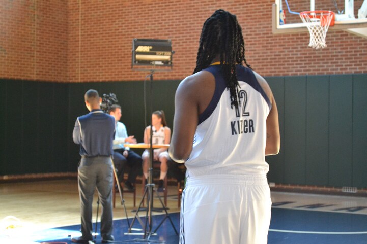 Lynetta Kizer watching from across the court as Maggie Lucas gets interviewed.