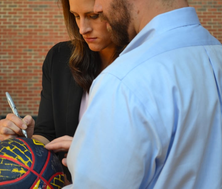 Head coach Stephanie White signs a blue, yellow and red Indiana Fever basketball with a silver Sharpie.