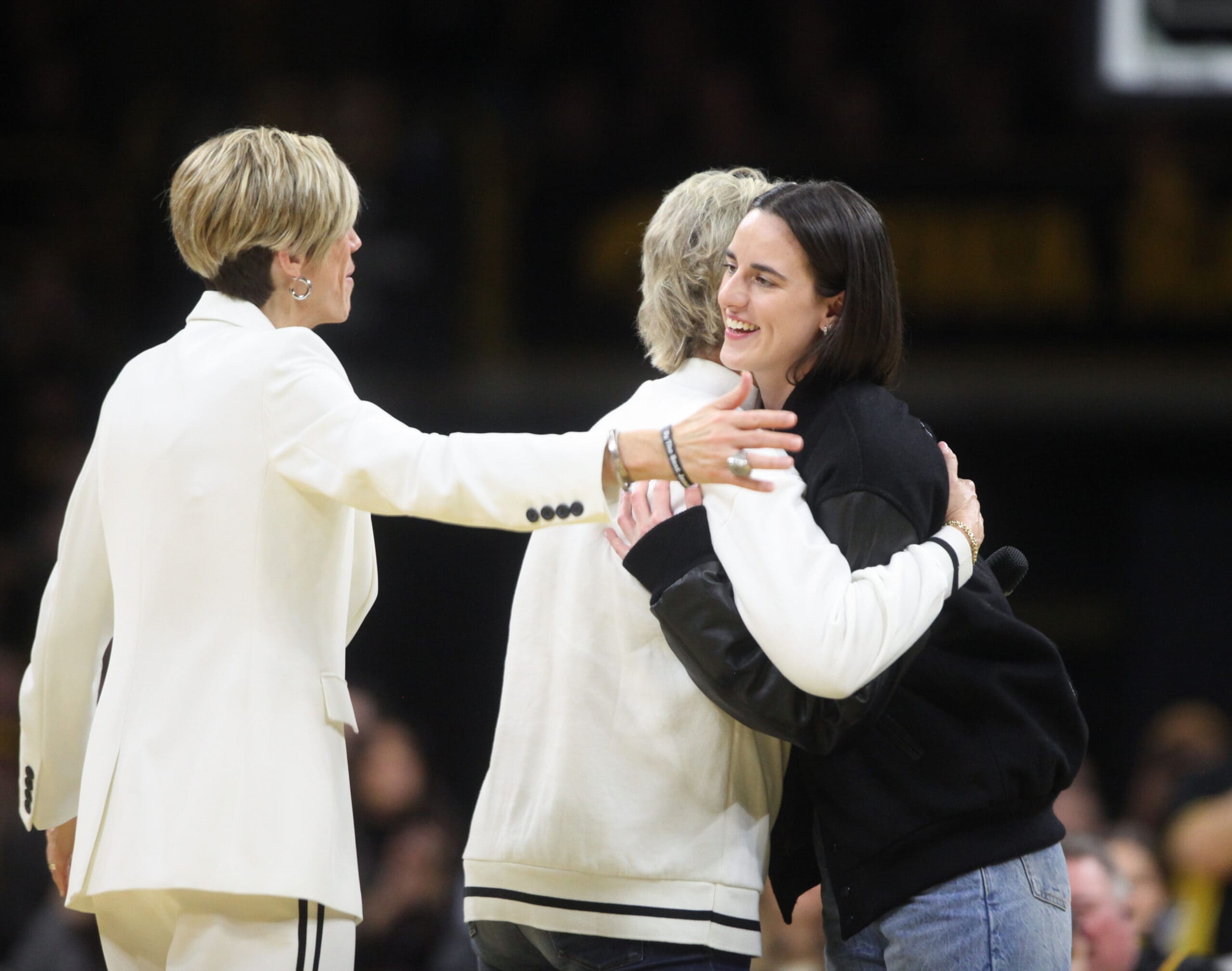 Caitlin Clark hugs former head coach Lisa Bluder and current University of Iowa head coach Jan Jensen before her jersey retirement ceremony